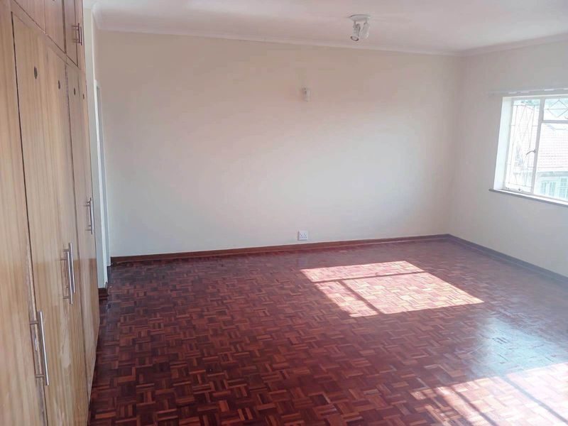 A spacious, empty bedroom featuring well-maintained parquet flooring and ample built-in cupboard storage, illuminated by natural light from the window.