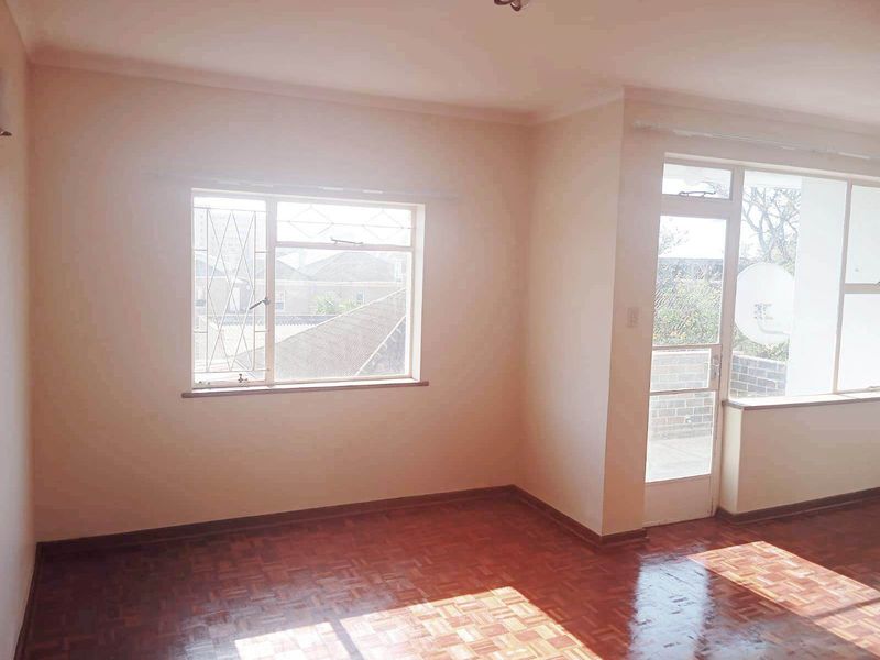 An empty living room featuring polished parquet flooring, natural light from large windows, and direct access to an adjoining balcony area.