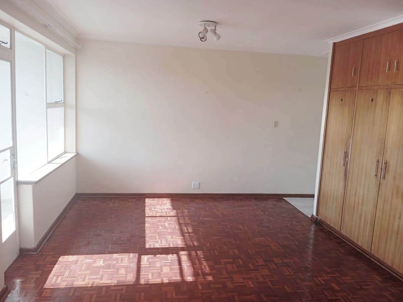 A bright, empty bedroom featuring classic parquet flooring, ample built-in wooden storage cupboards, and large windows allowing for natural light.