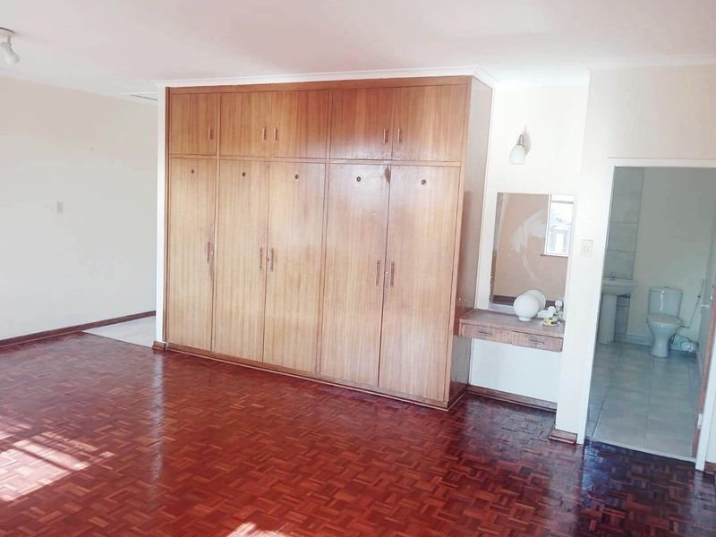 Spacious bedroom featuring classic parquet flooring, extensive built-in wooden wardrobes, and an integrated vanity area with direct access to an en-suite bathroom.
