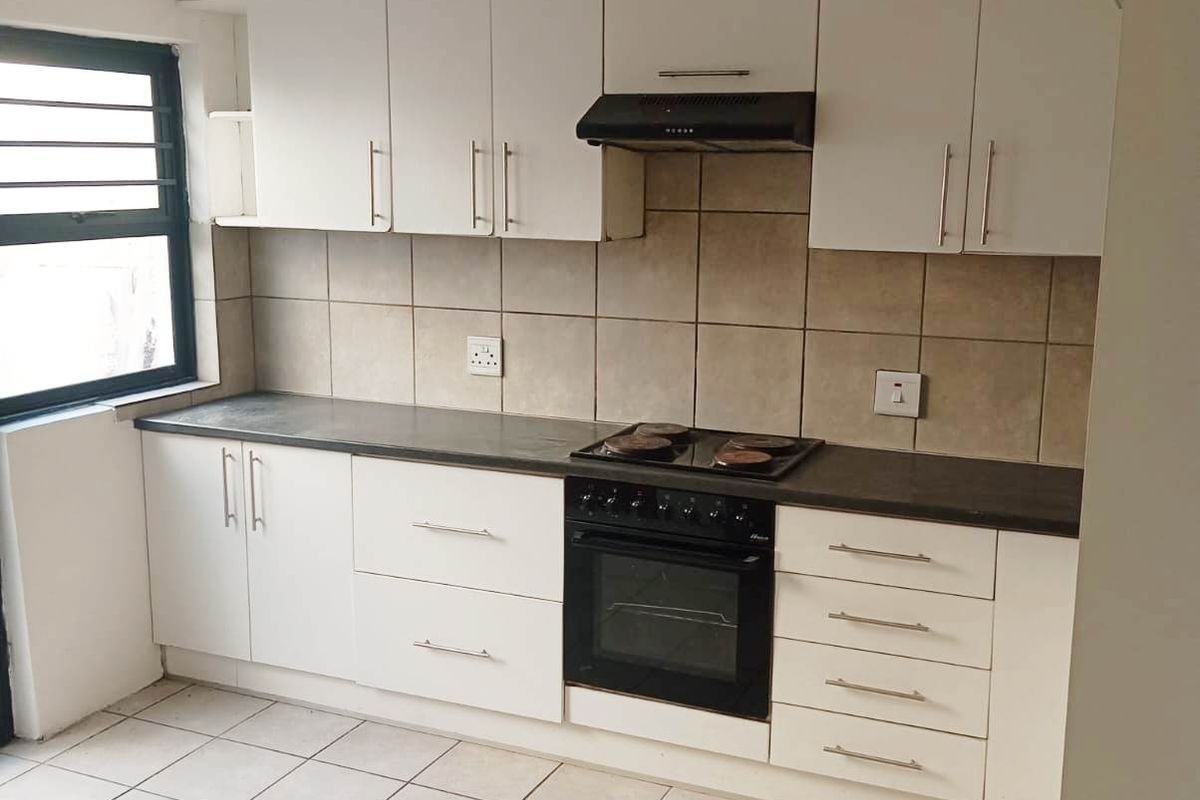 A functional kitchen featuring white cabinetry, dark countertops, built-in oven and hob, extractor fan, and neutral tiled flooring.