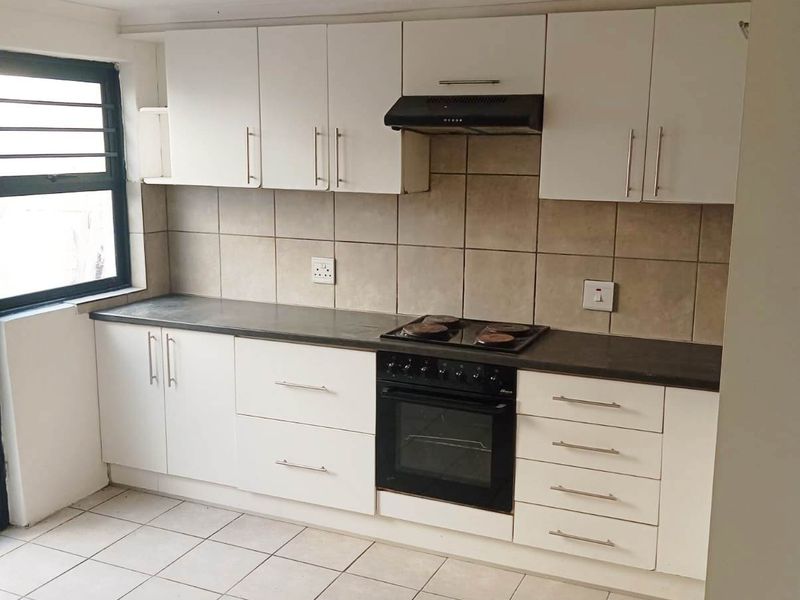 A functional kitchen featuring white cabinetry, dark countertops, built-in oven and hob, extractor fan, and neutral tiled flooring.