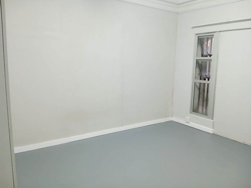A clean, empty bedroom featuring neutral walls, grey flooring, and a vertical casement window with white trim.