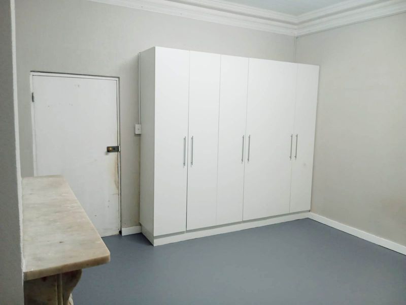 A clean, empty bedroom featuring a large white built-in wardrobe, crown molding, and neutral grey flooring.