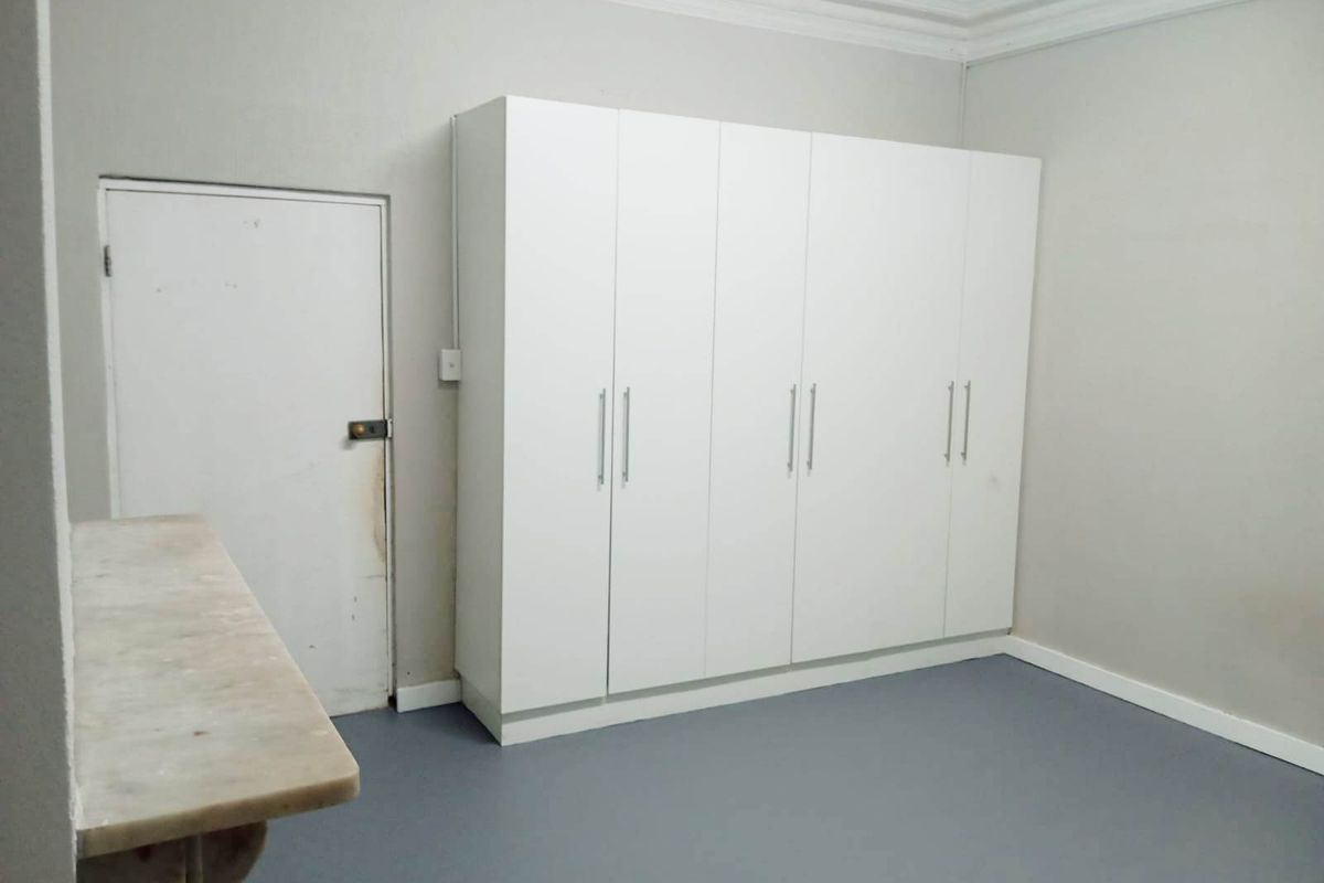 A clean, empty bedroom featuring a large white built-in wardrobe, crown molding, and neutral grey flooring.
