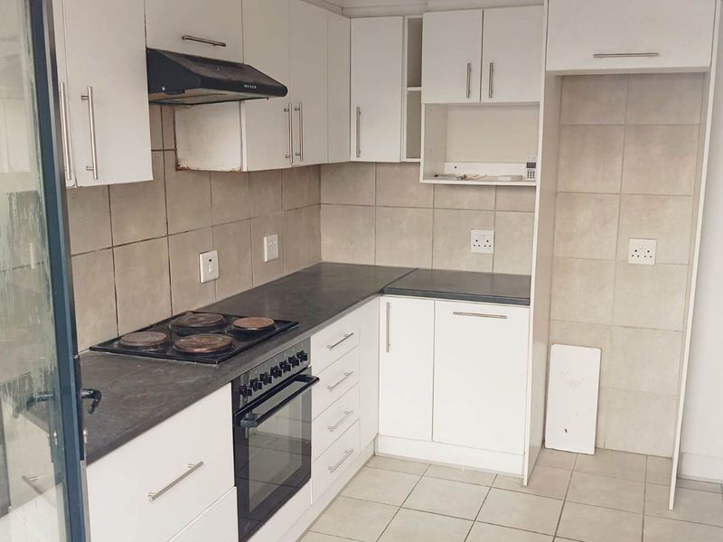 A functional kitchen featuring white built-in cabinetry, dark laminate countertops, an integrated electric oven and hob, and neutral tiled flooring.