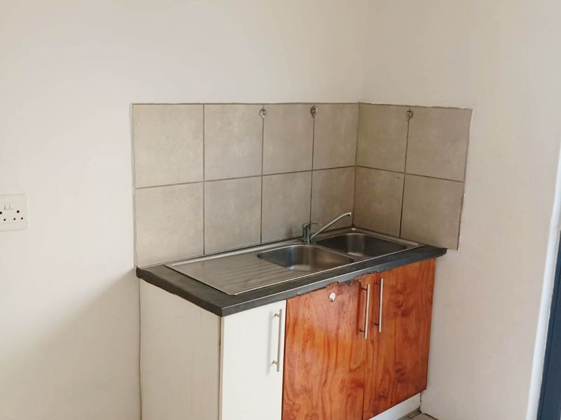 A compact kitchen area featuring a stainless steel sink, tiled splashback, and base cabinetry, currently in need of cosmetic updates.