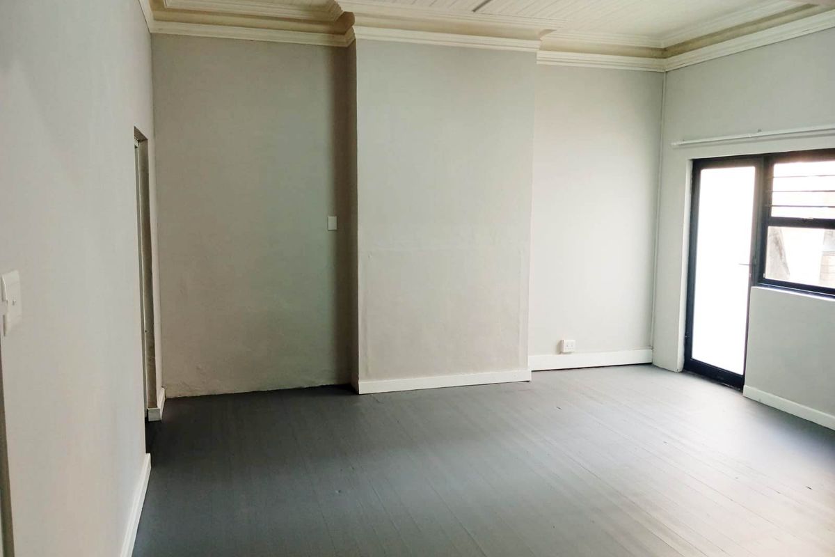 An empty living room featuring painted timber flooring, decorative ceiling cornices, and a glass door providing natural light.