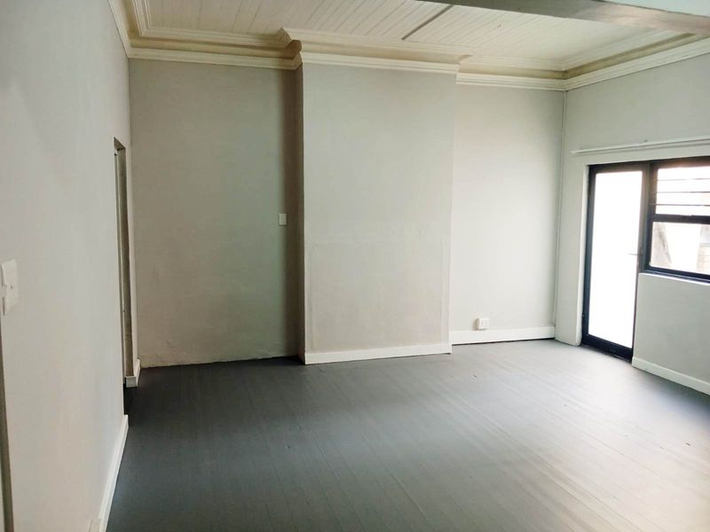 An empty living room featuring painted timber flooring, decorative ceiling cornices, and a glass door providing natural light.