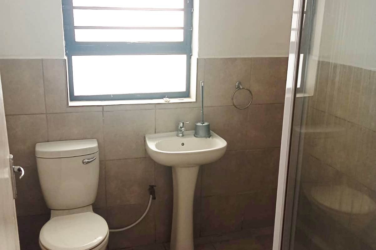 A functional bathroom featuring a pedestal basin, toilet, and a glass-enclosed shower with neutral wall and floor tiling.