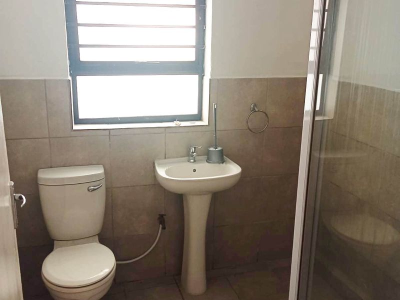 A functional bathroom featuring a pedestal basin, toilet, and a glass-enclosed shower with neutral wall and floor tiling.