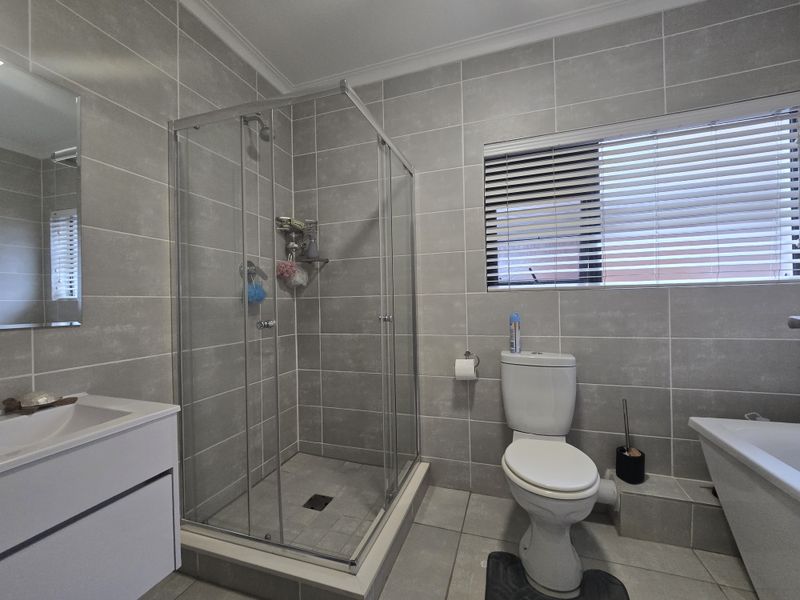 Modern bathroom featuring a glass shower enclosure, wall-mounted vanity, bathtub, and neutral grey floor-to-ceiling tiling.