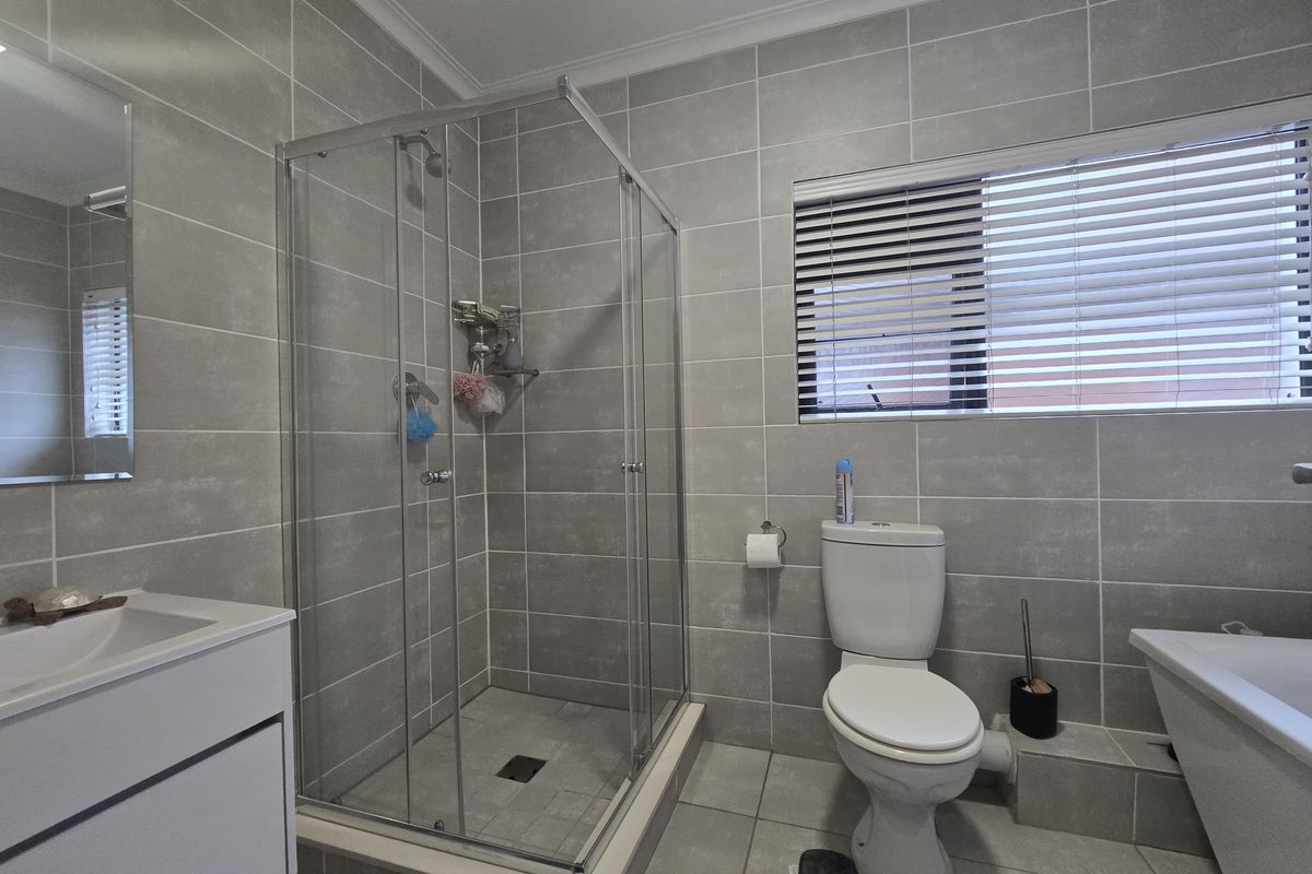 Modern bathroom featuring a glass shower enclosure, wall-mounted vanity, bathtub, and neutral grey floor-to-ceiling tiling.