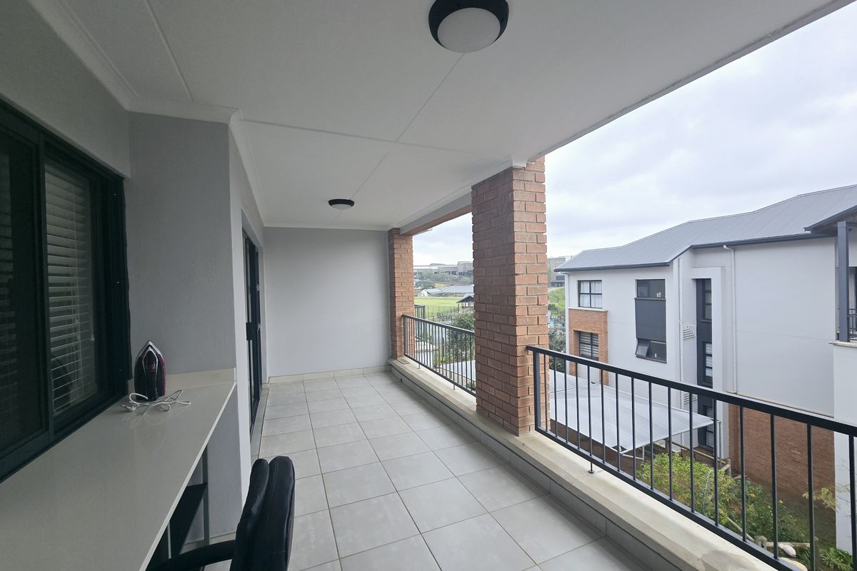 A spacious covered balcony featuring tiled flooring, exposed brick pillars, a metal balustrade, and a convenient built-in counter area.