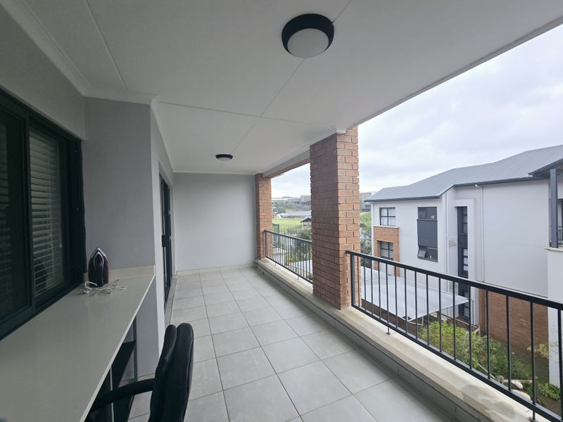 A spacious covered balcony featuring tiled flooring, exposed brick pillars, a metal balustrade, and a convenient built-in counter area.