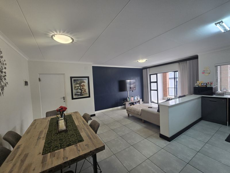 Spacious open-plan living and dining area featuring tiled flooring, a breakfast bar, and direct access to a balcony through sliding glass doors.
