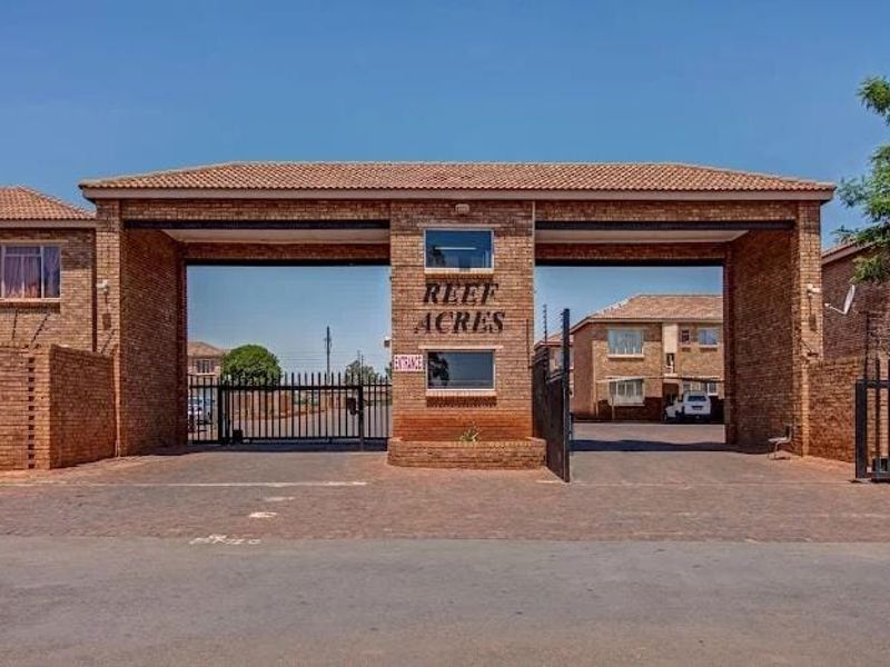 The main entrance to Reef Acres apartment complex, featuring a brick facade, security gate, and paved driveway access.