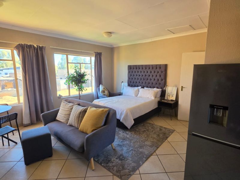 Open-plan studio apartment featuring tiled flooring and large windows, providing a functional living and sleeping space.