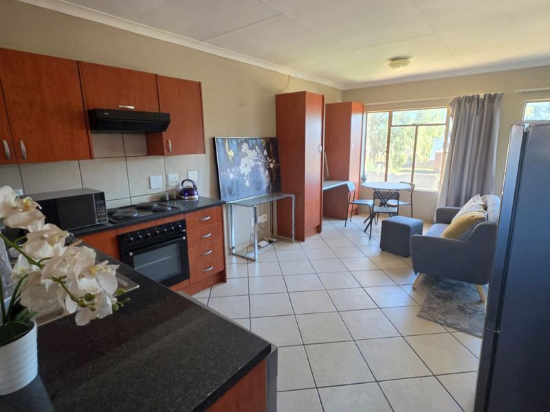Open-plan kitchen and living area featuring tiled flooring, wooden cabinetry, and granite countertops, with natural light from a large window.