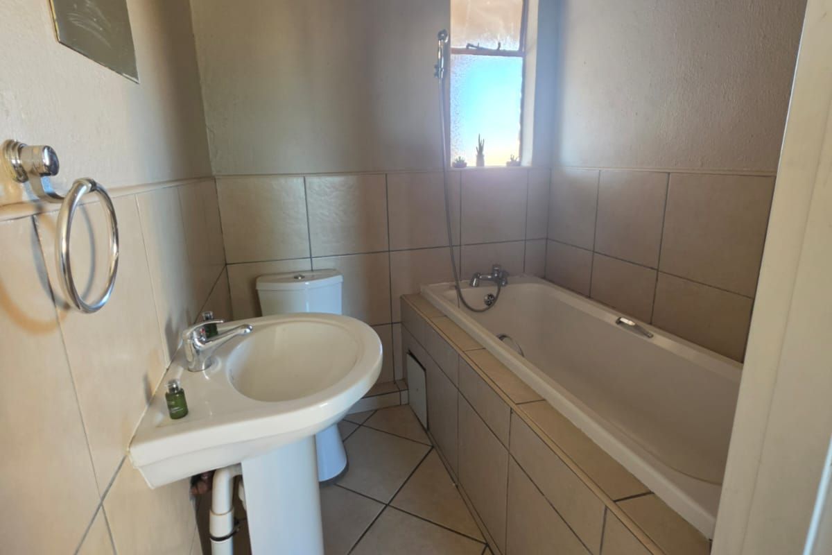 A functional bathroom featuring a pedestal basin, bathtub, and toilet with neutral wall and floor tiling.