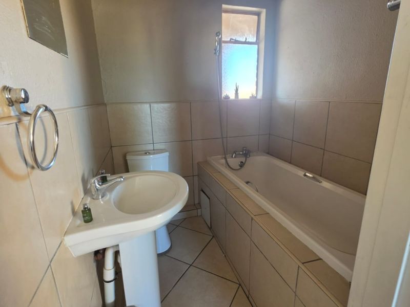 A functional bathroom featuring a pedestal basin, bathtub, and toilet with neutral wall and floor tiling.