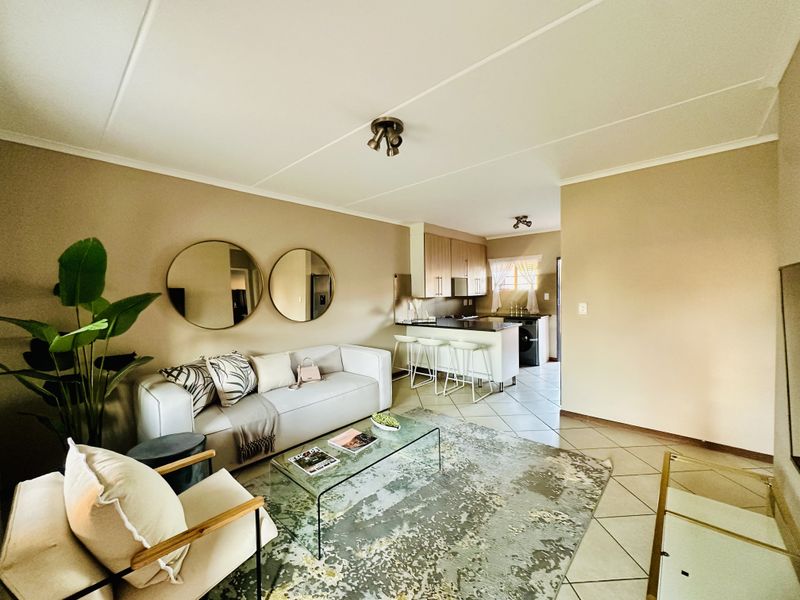 An open-plan living area featuring a modern kitchen with cabinetry and an island, seamlessly flowing into a comfortable lounge space with tiled flooring.