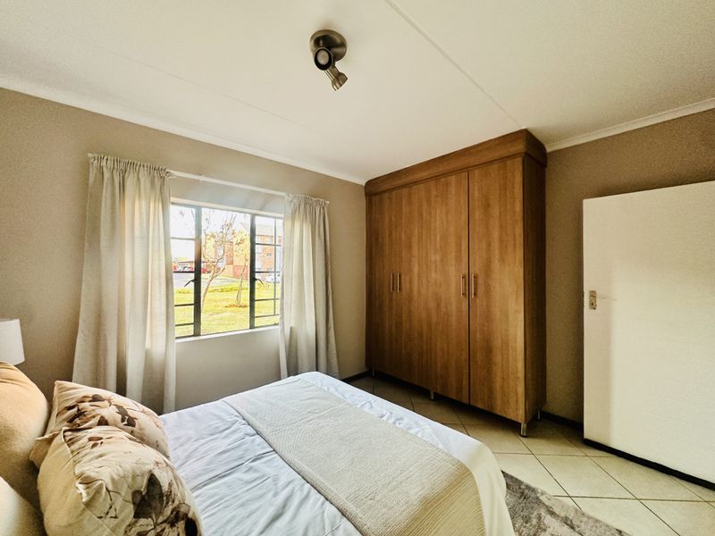 A well-maintained bedroom featuring tiled flooring, a large built-in wooden wardrobe, and a window with security bars overlooking the exterior grounds.