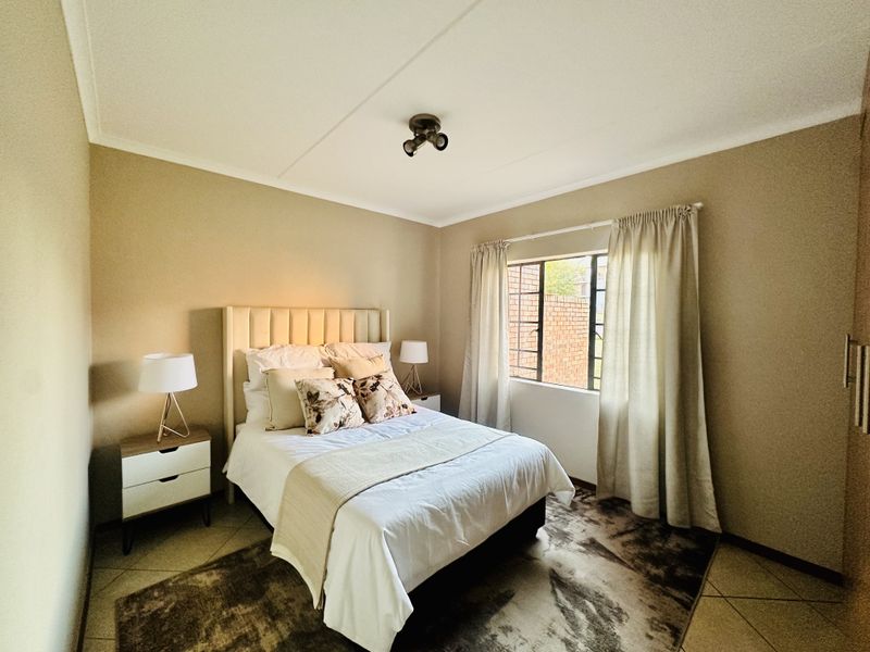 A well-maintained bedroom featuring neutral wall tones, tiled flooring, a built-in wardrobe, and a window fitted with security bars.
