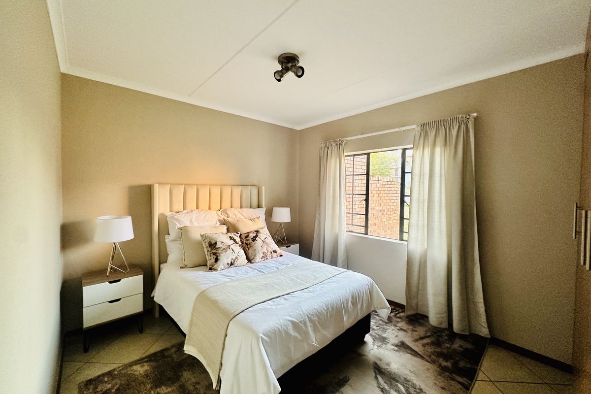 A well-maintained bedroom featuring neutral wall tones, tiled flooring, a built-in wardrobe, and a window fitted with security bars.