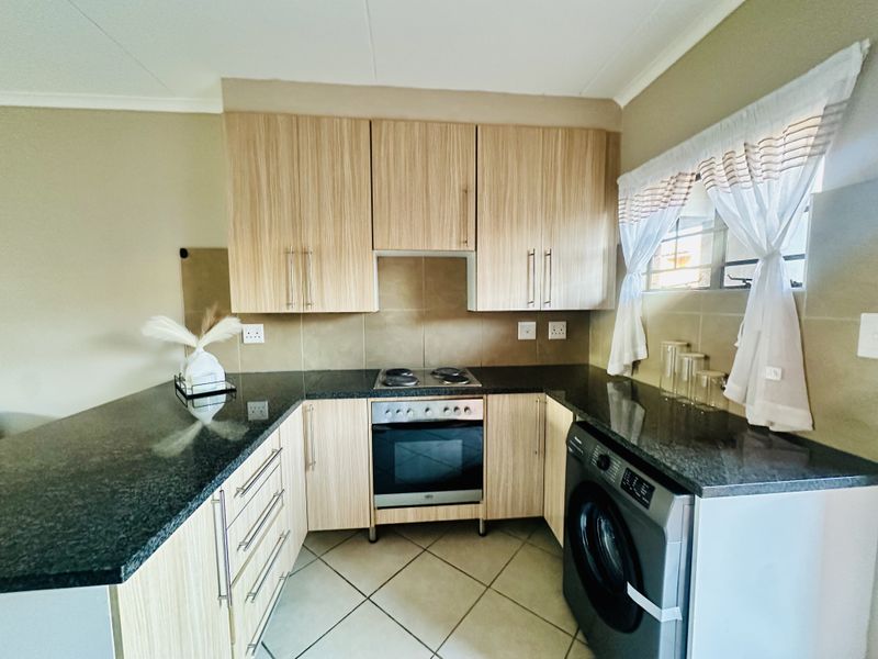 A functional kitchen featuring light wood-finish cabinetry, dark granite countertops, a built-in oven with electric hob, and tiled flooring.
