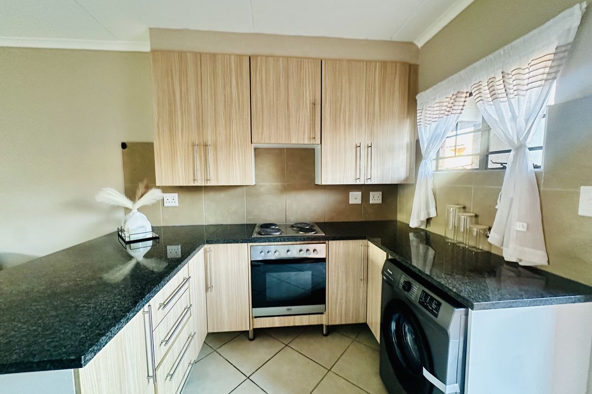 A functional kitchen featuring light wood-finish cabinetry, dark granite countertops, a built-in oven with electric hob, and tiled flooring.