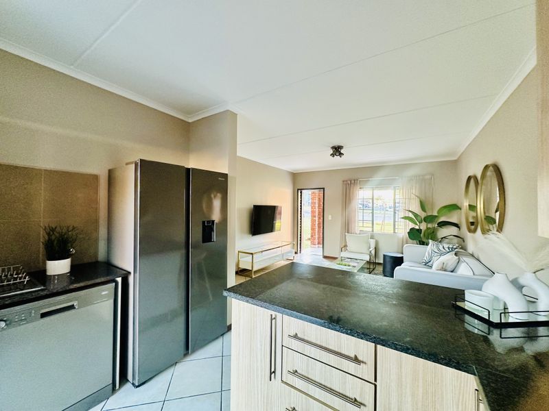 Open-plan living area featuring a modern kitchen with granite countertops, island, and tiled flooring, seamlessly flowing into the adjacent lounge space.