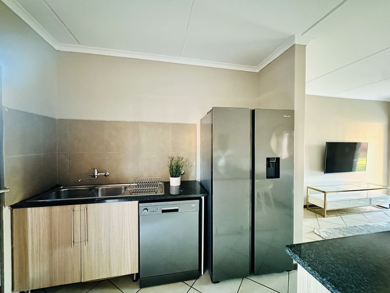 Open-plan kitchen area featuring modern cabinetry, tiled backsplash, double sink, and integrated dishwasher, seamlessly flowing into the adjacent living space.