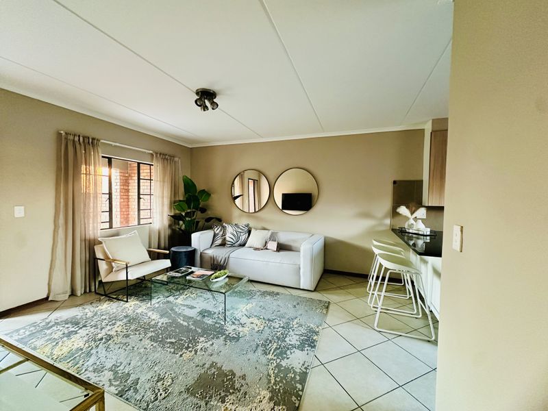An open-plan living and kitchen area featuring tiled flooring, a breakfast bar, and neutral wall tones, creating a functional and cohesive living space.