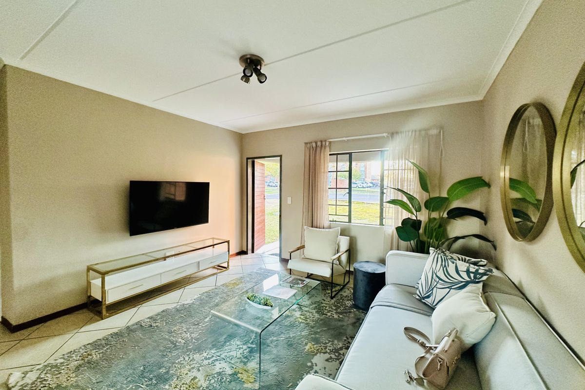 A well-maintained living room featuring tiled flooring, neutral wall tones, and a window with security bars, providing a bright and functional living space.