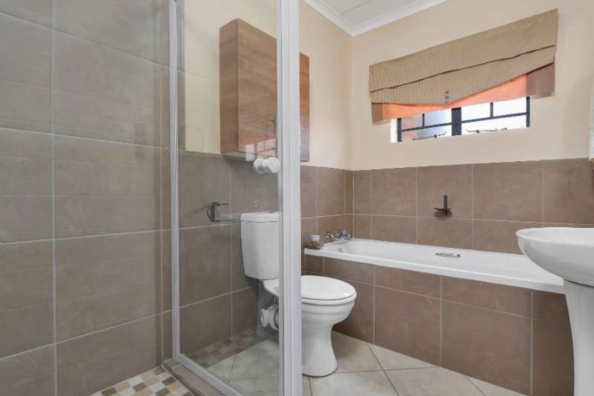 A functional bathroom featuring a shower enclosure, built-in bathtub, pedestal basin, and toilet with neutral wall and floor tiling.