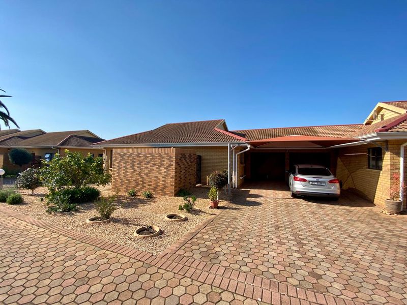 Front view of a brick house featuring a paved driveway, carport, and low-maintenance landscaped garden area.