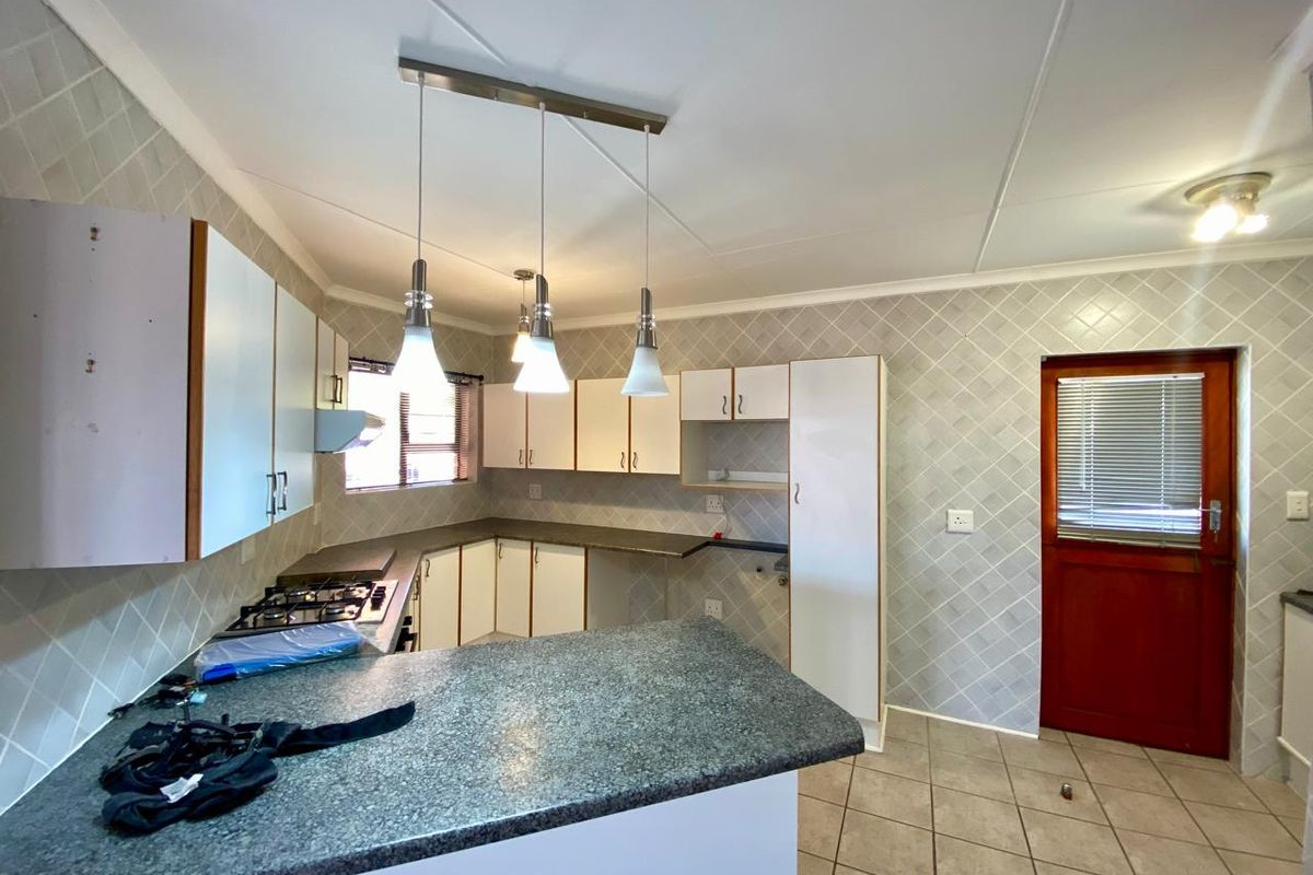 A functional kitchen featuring built-in cabinetry, laminate countertops, a gas hob with extractor fan, and tiled splashbacks with direct exterior access.
