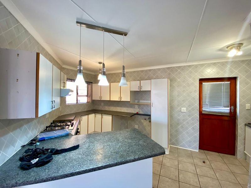 A functional kitchen featuring built-in cabinetry, laminate countertops, a gas hob with extractor fan, and tiled splashbacks with direct exterior access.