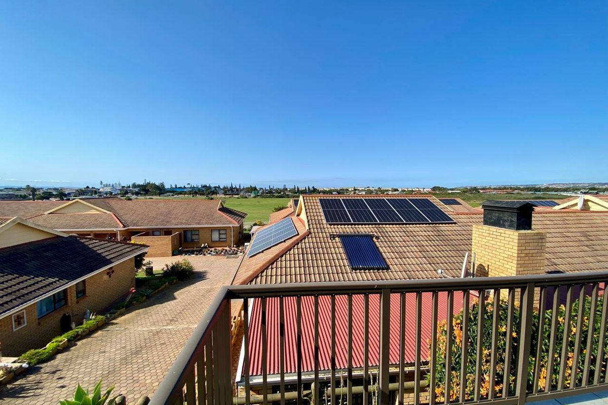 Elevated view overlooking a residential complex featuring tiled roofs, solar energy installations, and a paved driveway area.