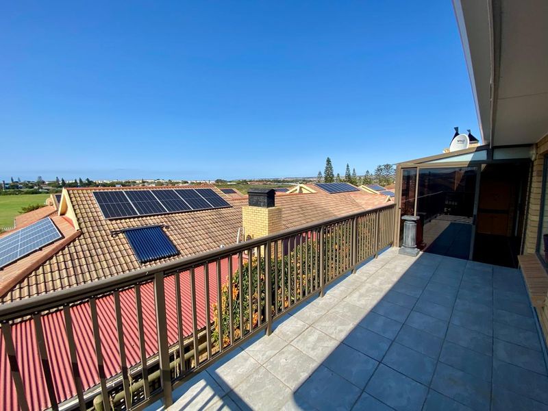 A spacious tiled balcony featuring a metal balustrade, offering elevated views over the surrounding neighborhood and rooftops equipped with solar energy systems.