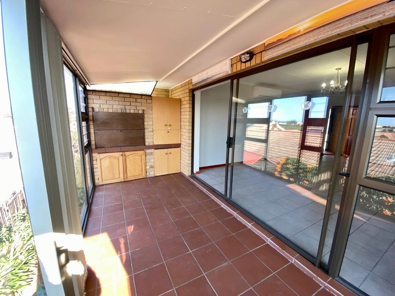 Enclosed patio area featuring tiled flooring, a built-in braai, and large sliding glass doors providing access to the main living space.