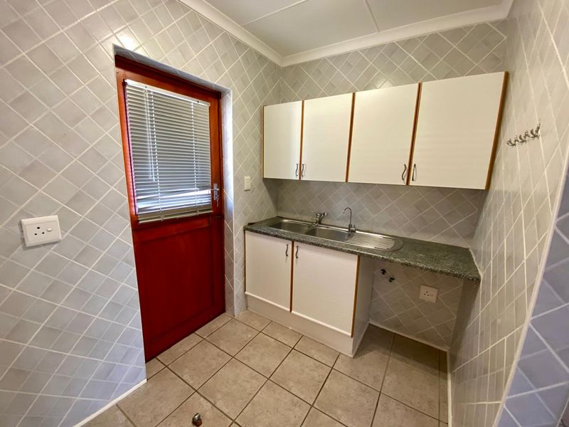A functional laundry room featuring built-in cabinetry, a stainless steel sink, tiled splashbacks, and direct access to the exterior.
