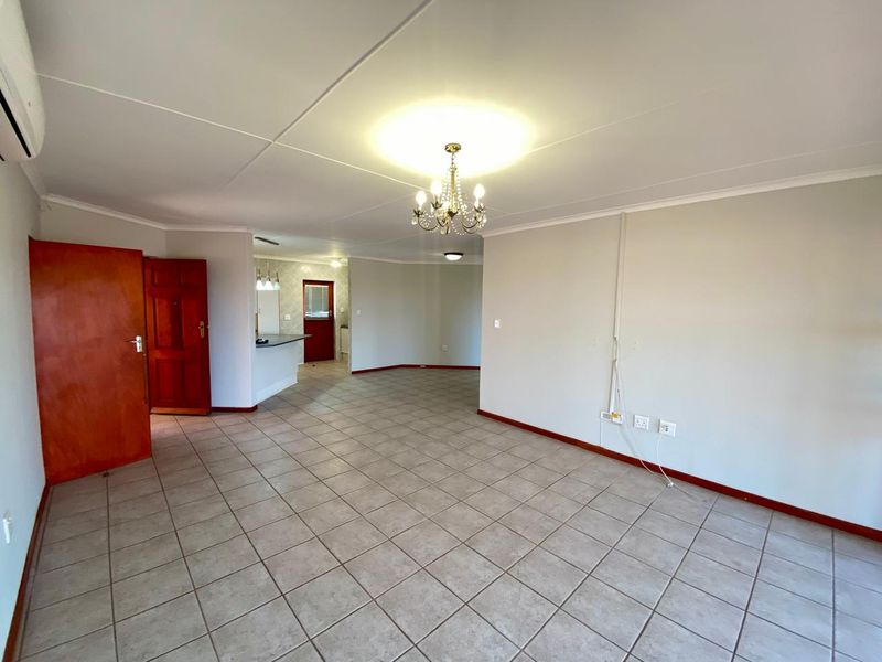 Spacious open-plan living area featuring neutral tiled flooring, coved ceilings, a central chandelier, and an integrated kitchen breakfast bar.