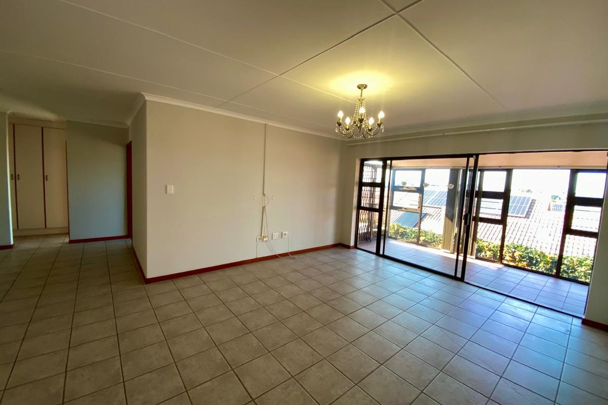 Spacious, empty living area featuring tiled floors, a central chandelier, and large sliding glass doors providing access to an outdoor balcony.