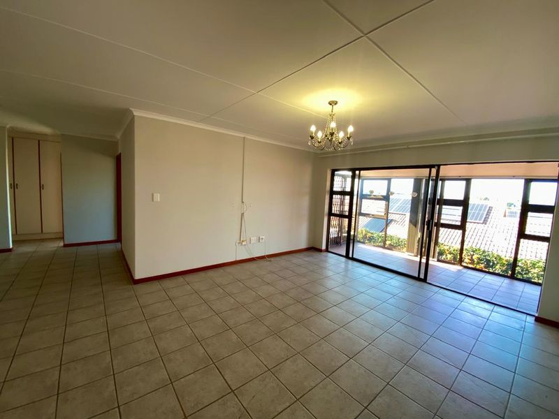 Spacious, empty living area featuring tiled floors, a central chandelier, and large sliding glass doors providing access to an outdoor balcony.