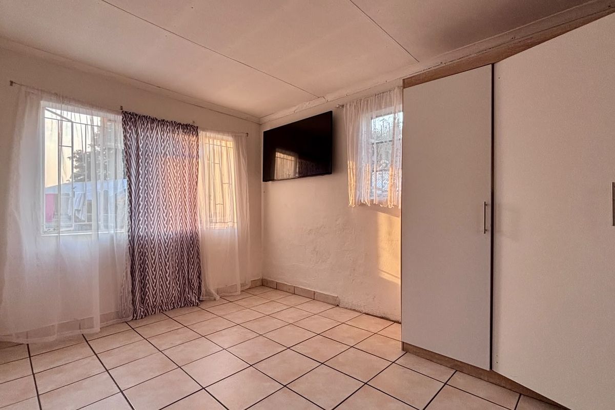 A bedroom featuring tiled flooring, built-in wardrobes, and security bars on the windows.