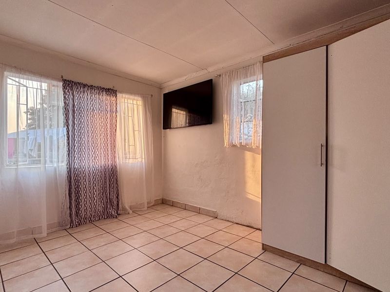 A bedroom featuring tiled flooring, built-in wardrobes, and security bars on the windows.