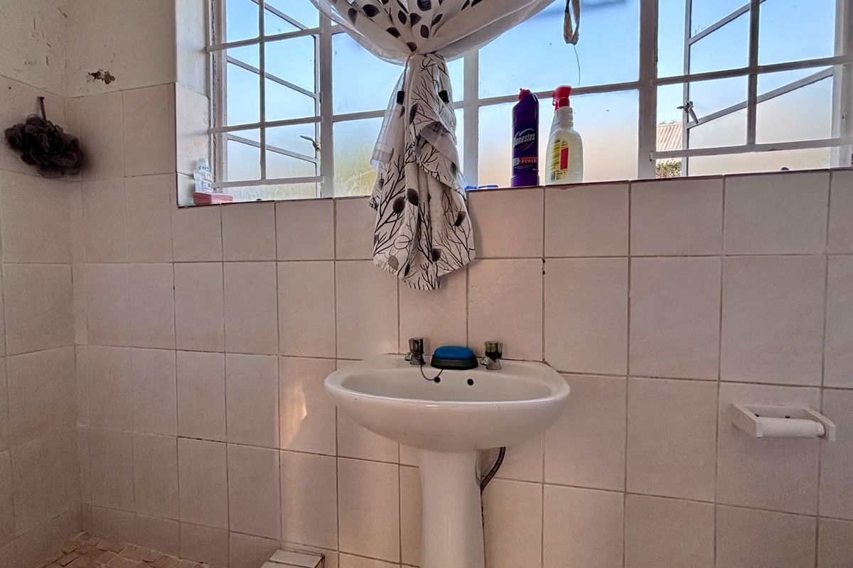 A functional bathroom featuring a pedestal basin, tiled walls, and a steel window frame, requiring some cosmetic updates to the finishes.