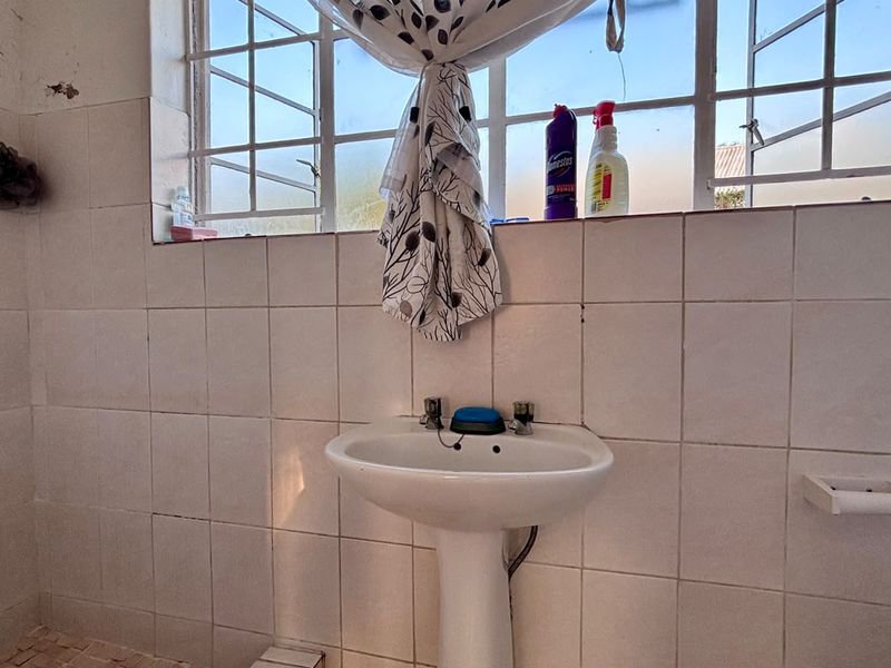 A functional bathroom featuring a pedestal basin, tiled walls, and a steel window frame, requiring some cosmetic updates to the finishes.